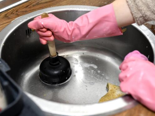 woman's hands with a plunger unclogging the kitchen drain